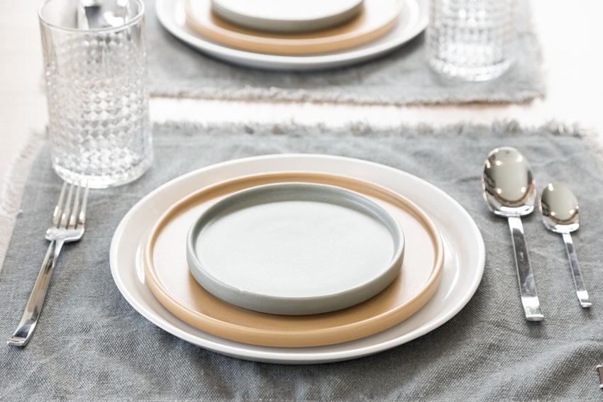 Ceramic plates on top of a table napkin with spoons, fork, and a glass