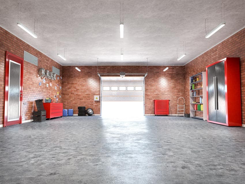 Garage with concrete floor, brick wall, tools, cabinets, and hanging lights