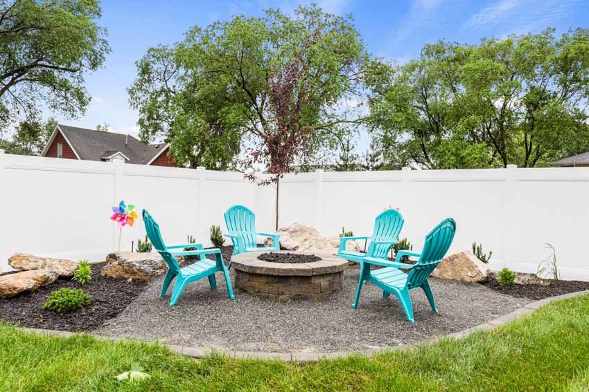 Crushed granite patio with fire pit, chairs, and vinyl fence