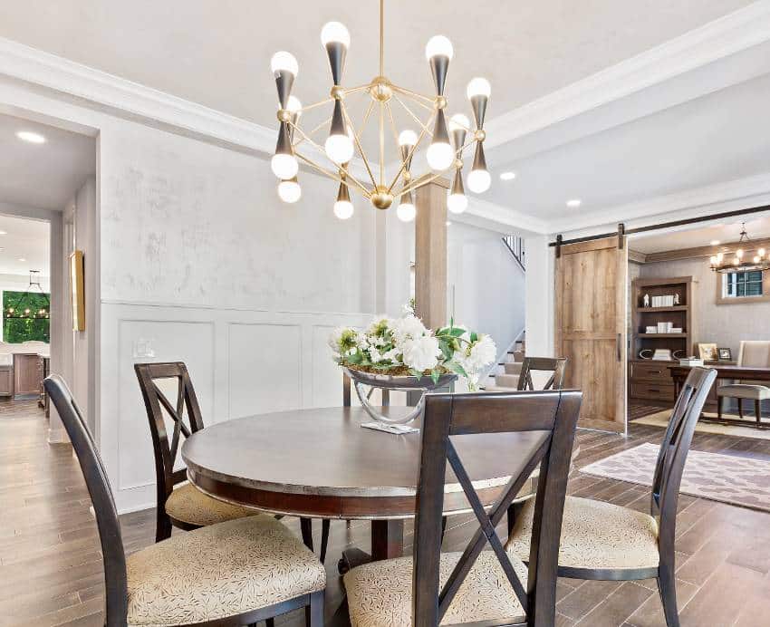 Dining area with small round wood table, modern chandelier with light bulbs and wood flooring