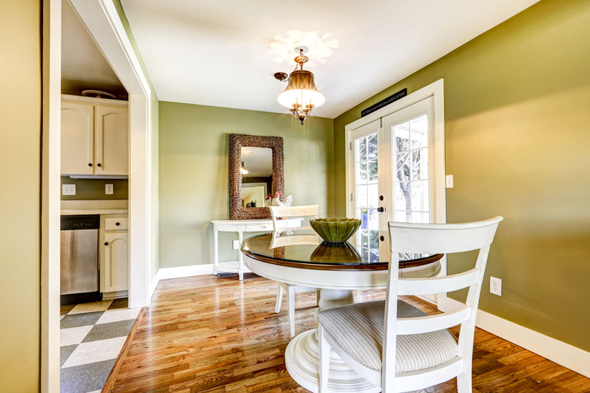Dining room with table, chairs, wood floor, olive green wall, mirror, and glass door