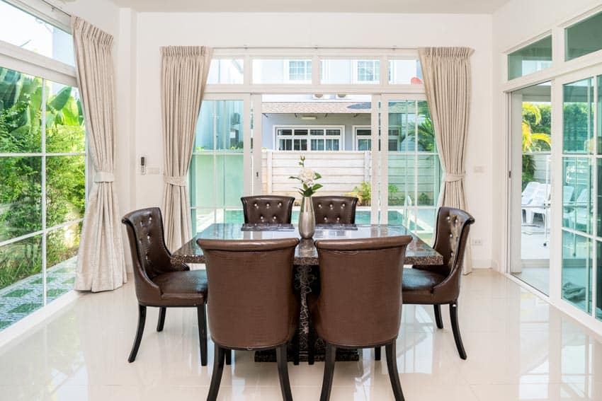 Dining room with table, leather cushioned chairs, glass door, windows, curtain, and quartz flooring