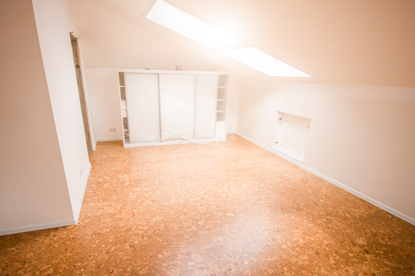 Empty attic with sloped ceiling, cork floors, and white walls