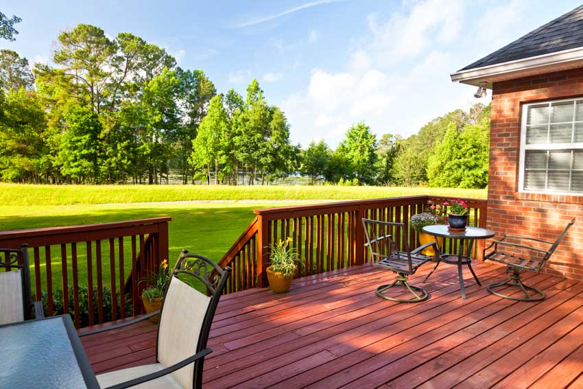 House exterior area with redwood deck, table, chairs, potted flowers, and railings