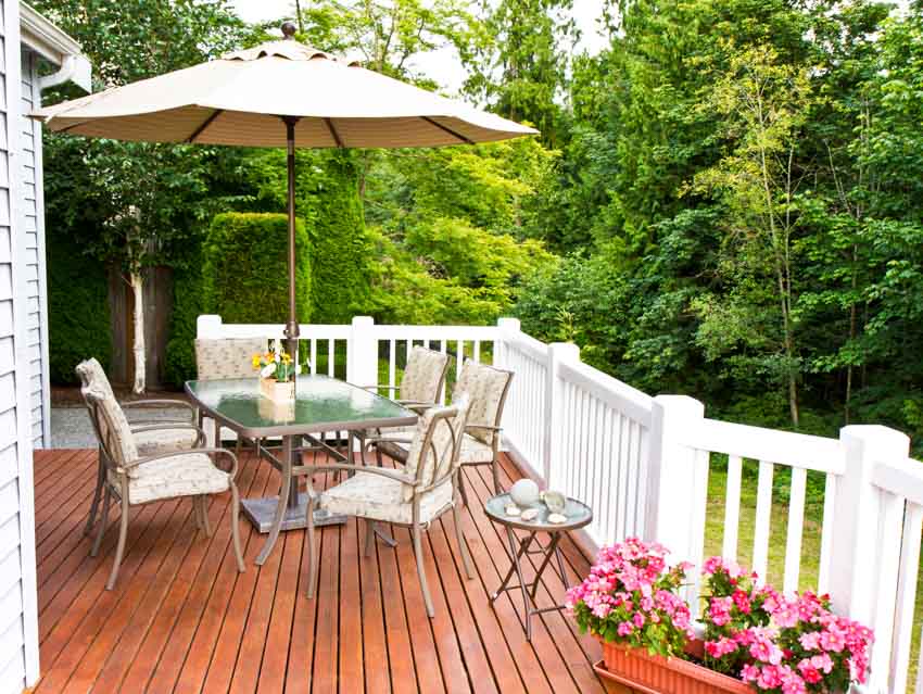 House exterior with redwood deck, patio umbrella shade, table, chairs, flowers, and white railings