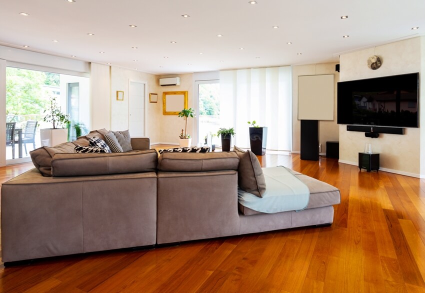 Huge living area with big brown sofa, wall mounted tv and mahogany floors