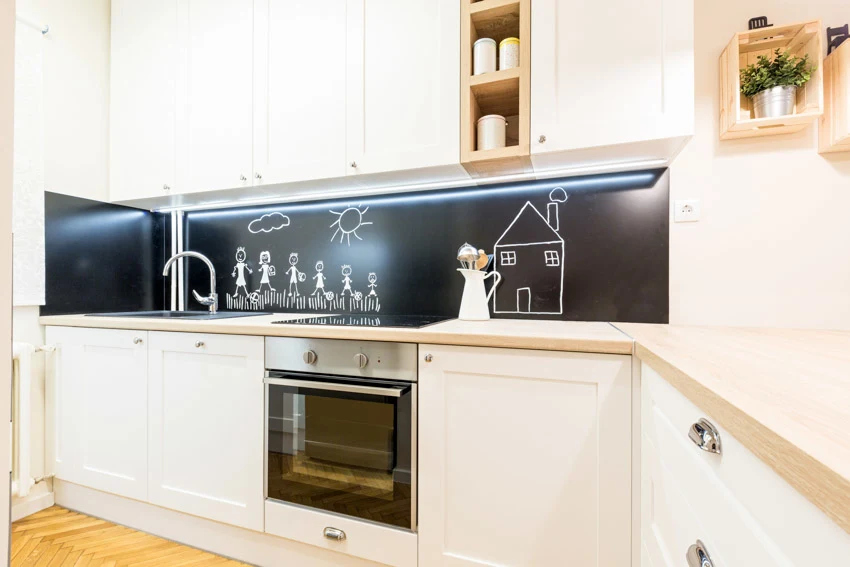 Industrial kitchen with chalkboard backsplash, countertop, white cabinets, and oven