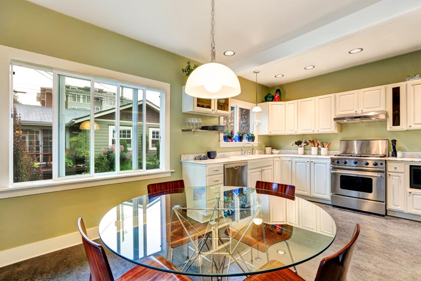 Kitchen and dining area with glass table, chairs, white cabinets, oven, stove, and windows
