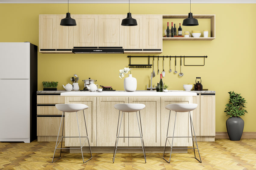 Kitchen with butter yellow walls, bar stools, cabinets, pendant lights, and floating shelves
