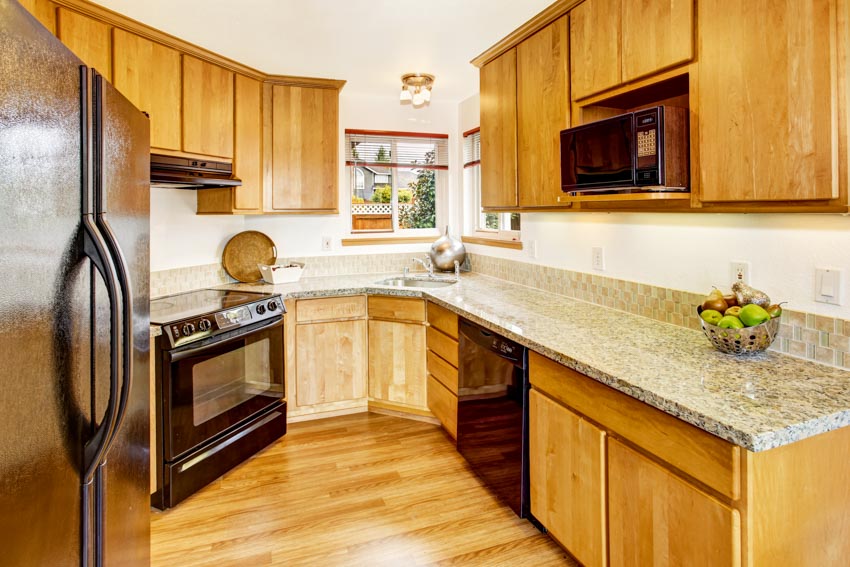 Kitchen with granite countertop, backsplash, particle board cabinets, oven, wood floor, and window