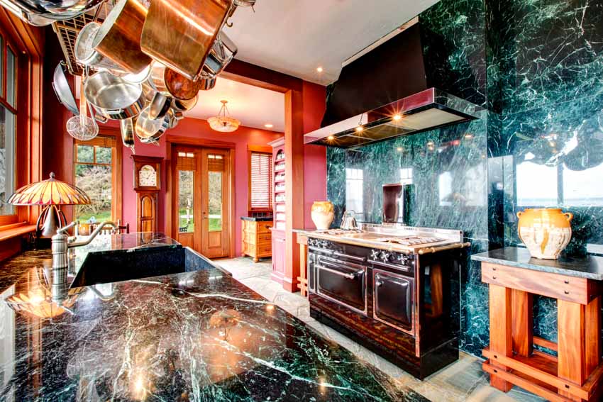 Kitchen with green onyx backsplash, countertops, range hood, stove, cabinets, and windows