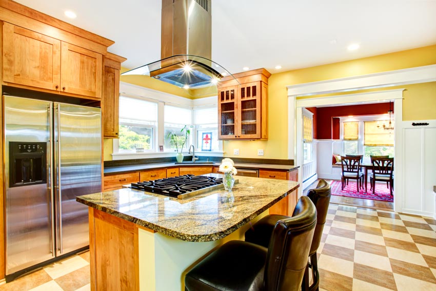 Kitchen with island, countertops, range hood, refrigerator, chairs, tile floors, and yellow walls