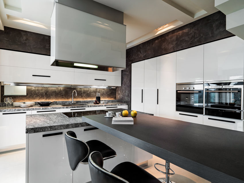 Kitchen with onyx backsplash, countertop, island, table, chairs, range hood, and cabinets