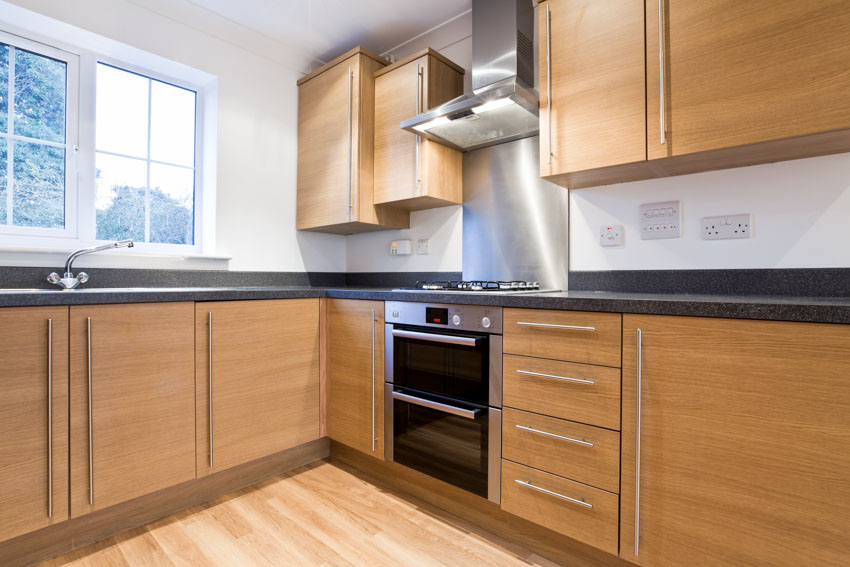 Kitchen with brown cabinets, backsplash, countertop, oven and window