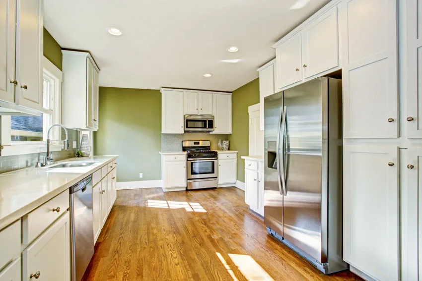 Kitchen with refrigerator, sage green wall, wood flooring, white cabinets, stove, oven, and countertops