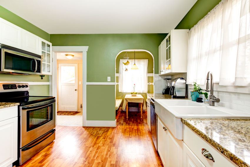 Kitchen with sage green wall, countertops, sink, wood floor, stove, oven, and window curtains