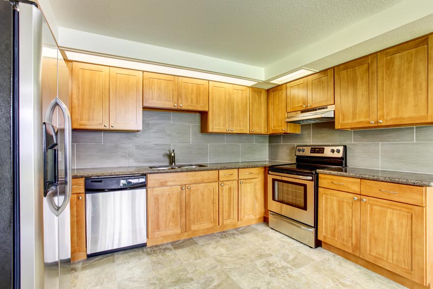Kitchen with tile backsplash, countertops, particle board cabinets, oven, dishwasher, and refrigerator