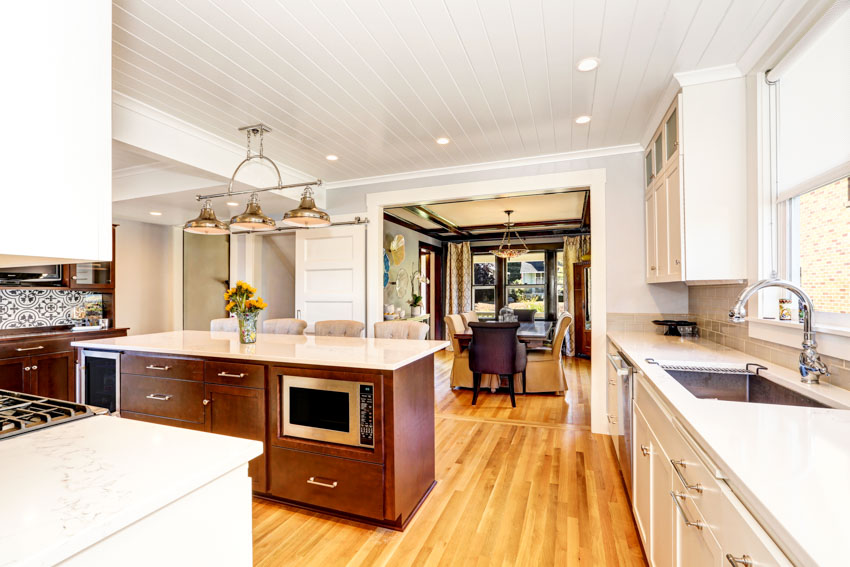 Kitchen with vinyl beadboard ceiling, island, countertops, pendant lights, sink, faucet, cabinets, windows, and wood floors