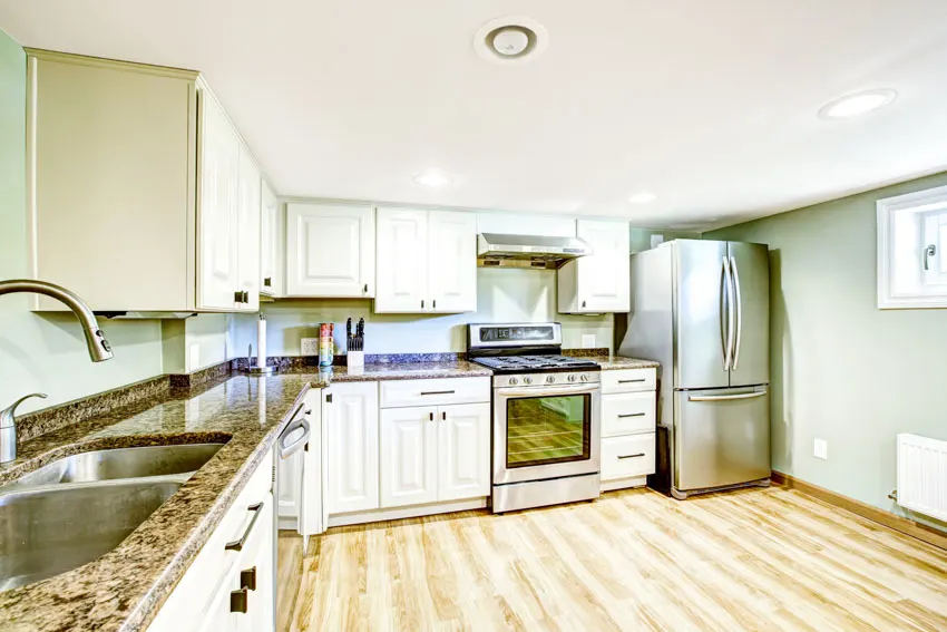 Kitchen with wood floor, white cabinets, sage green wall, countertop, sink, refrigerator, oven, and stove