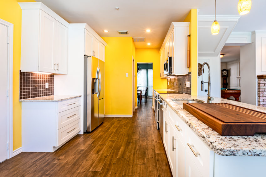 Kitchen with yellow walls, wood floor, countertops, backsplash, and white cabinets