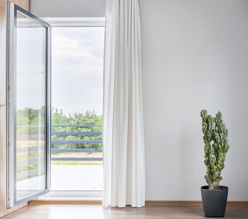 Bright room with open pivot door to balcony and cactus in pot standing on the floor