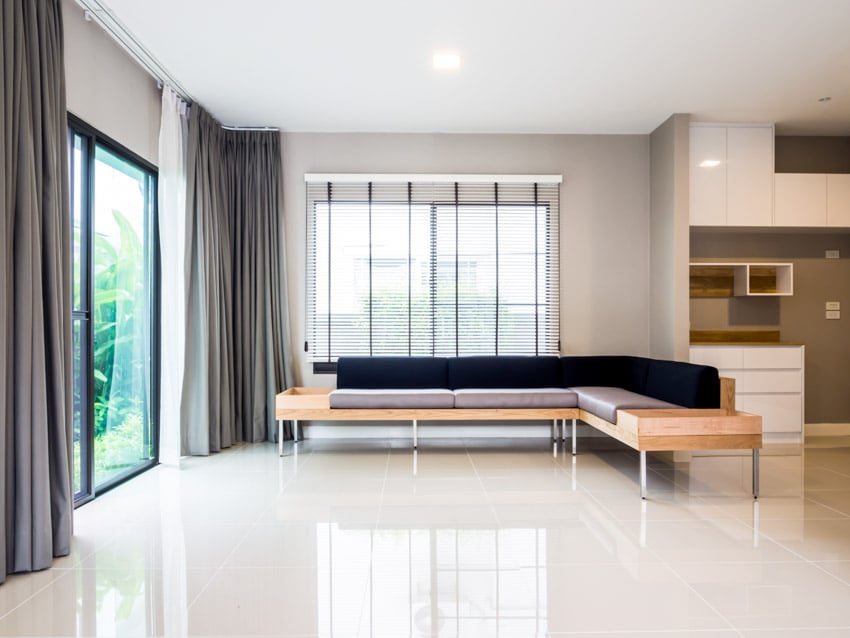 Living room with L shaped sofa, glass sliding door, curtains, windows, and quartz flooring