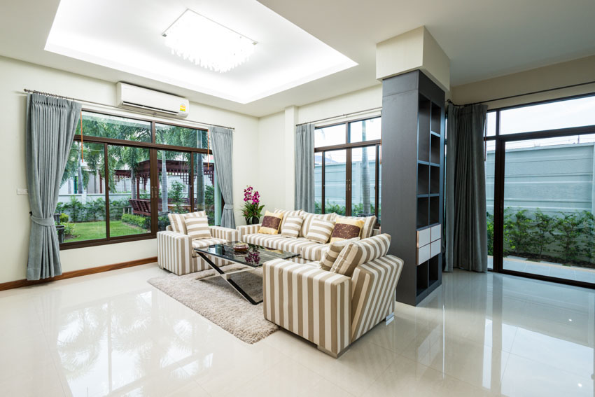 Living room with high gloss floor tiles, sofa chairs, couch, bookcase, windows, curtains, and glass door