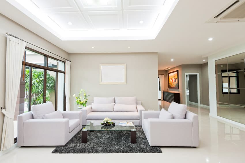 Room with sofa, love seats, grey area rug and center table with glass top