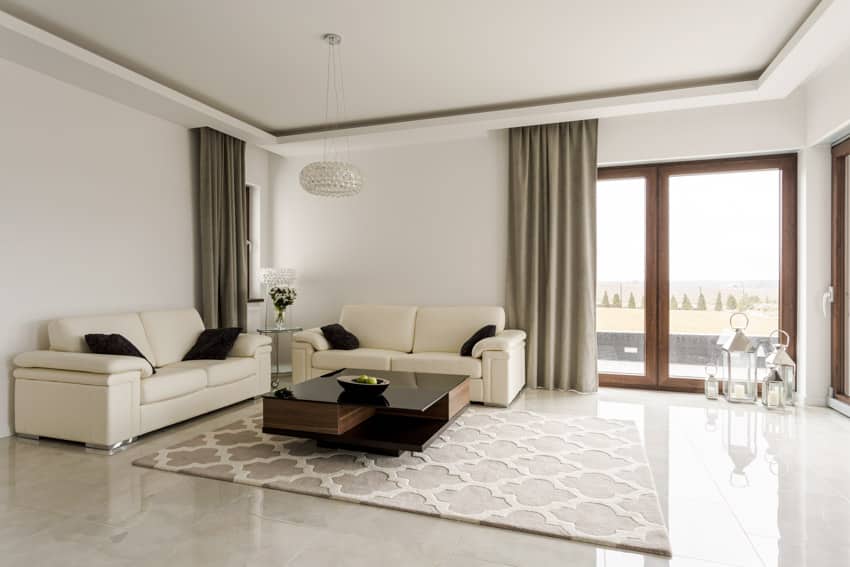 Living room with white leather sofas, coffee table, rug, windows, curtains, and quartz flooring