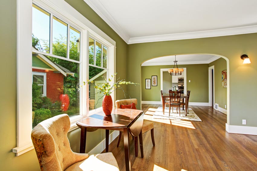Living room with windows, wood floor, table, chairs, and olive green wall