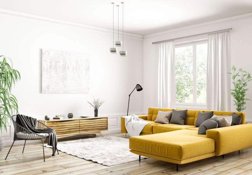 Гостиная с желтым секционным диваном, карнизом для штор, окном, консольным столиком, акцентным стулом, деревянным полом, ковром и комнатными растениями