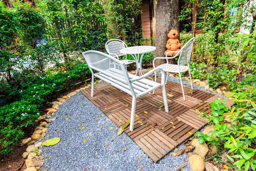 Modern patio with wood tiles, gravel, table, chairs, plants, and trees