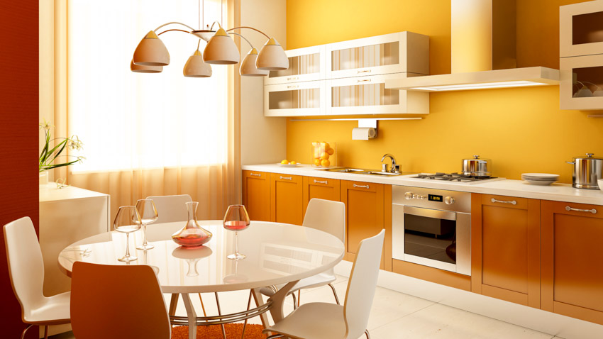 Modern kitchen with yellow walls, cabinets, round table, chairs, countertop, oven, and window curtains