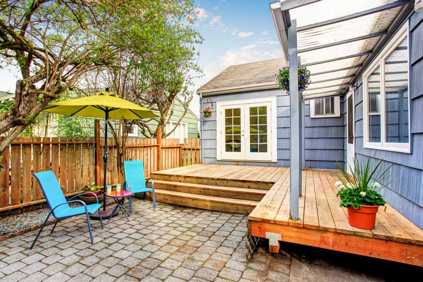 Outdoor area with pressure treated wood deck, canopy roof, paved patio, chairs, umbrella shade, and wooden fences