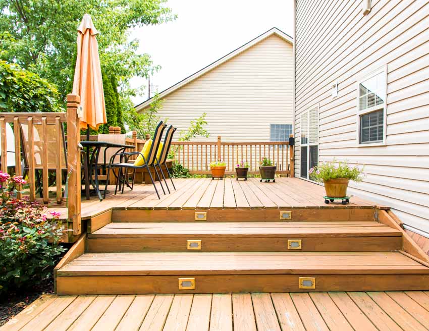 Outdoor area with pressure treated wood deck, railing, house siding, patio, umbrella, and chairs