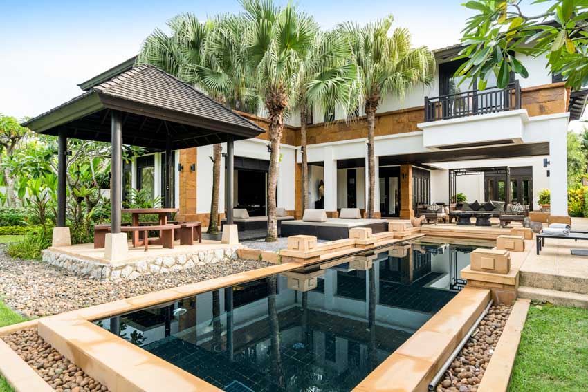 Outdoor area with swimming pool deck, palm trees, table, chairs, and backyard ramada