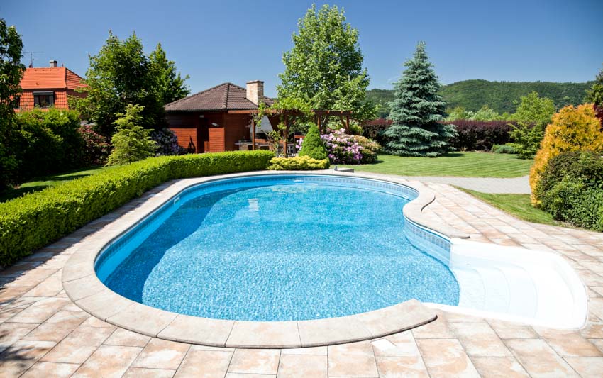 Outdoor area with swimming pool, trees, hedge plants, and limestone pool deck
