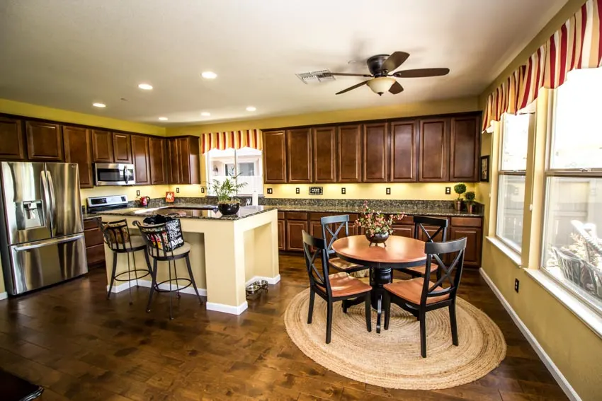 Spacious kitchen with dining area, table, chairs, island, yellow walls, cabinets, backsplash, curtains, and windows