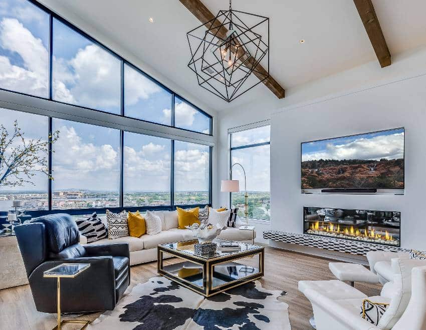Stunning living room with wood floors, glass wall, high awning windows and wood beams with modern metal chandelier