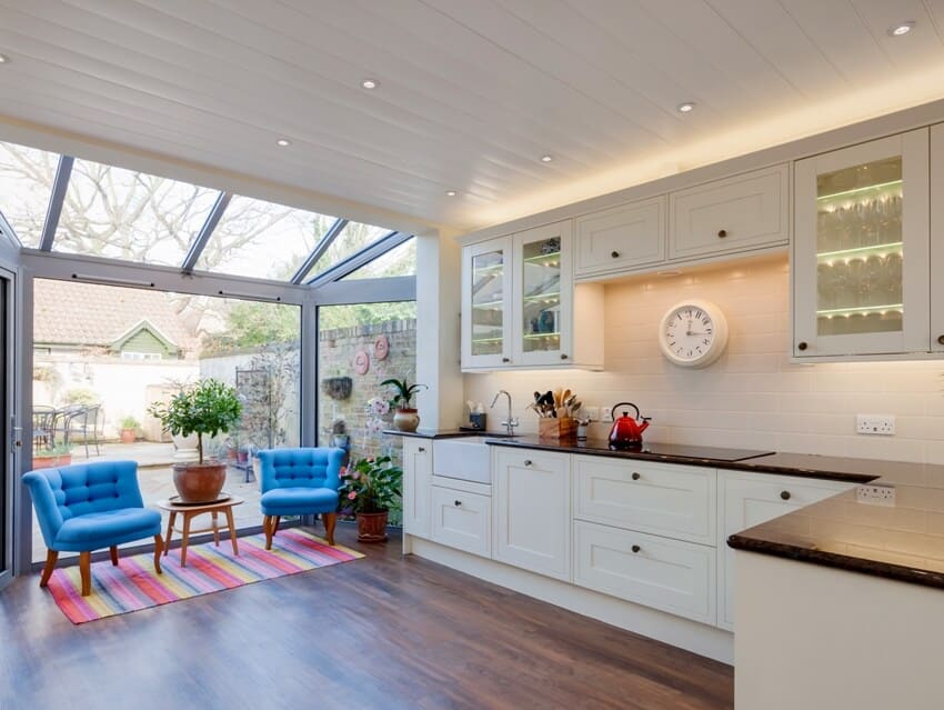 A traditional style kitchen with pvc panels ceiling, two blue armchairs and large window leading to rear garden and patio