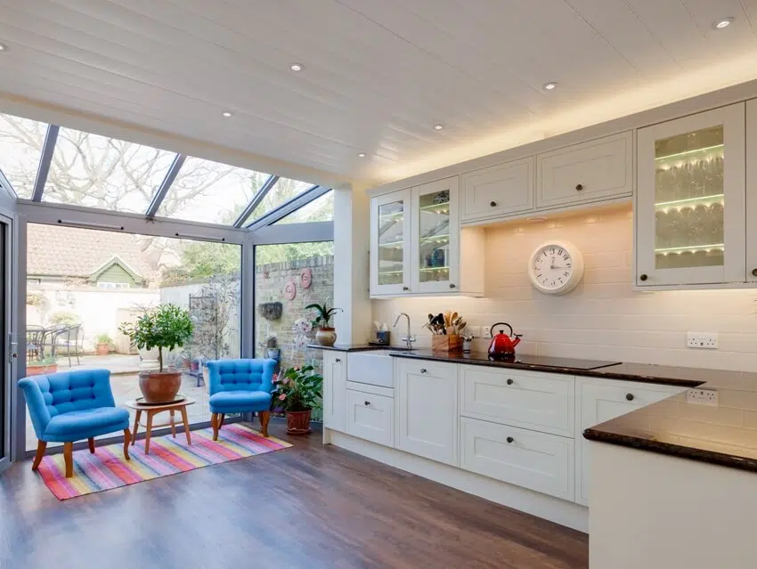 Kitchen with pvc panels ceiling, two blue armchairs and view of rear garden and patio 