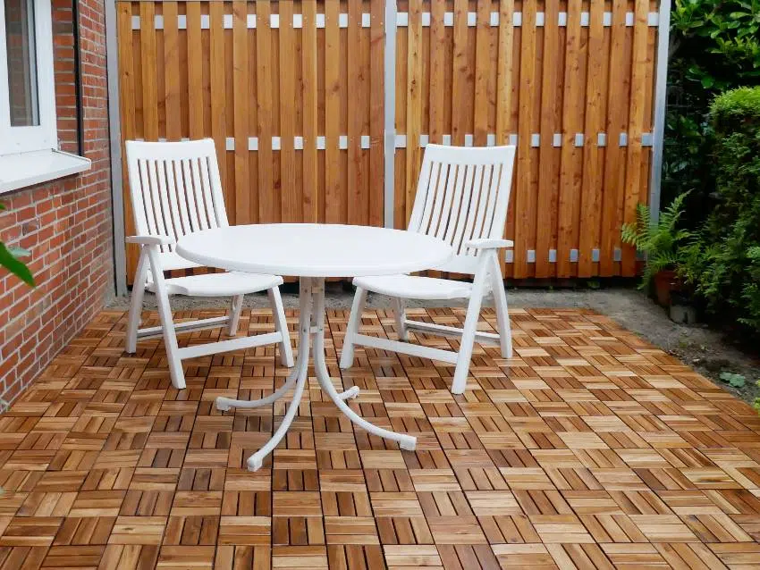 Two white garden chairs and a round table on the terrace with-teak wood deck tiles 