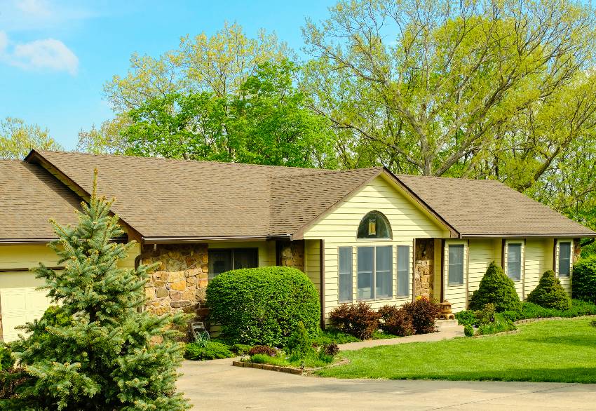 A view of ranch exterior with a mushroom bisque paint with beautiful landscape and trees on sunny spring day 