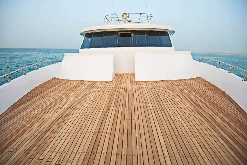 View over the bow with marine teak decking of a large luxury yacht on open ocean