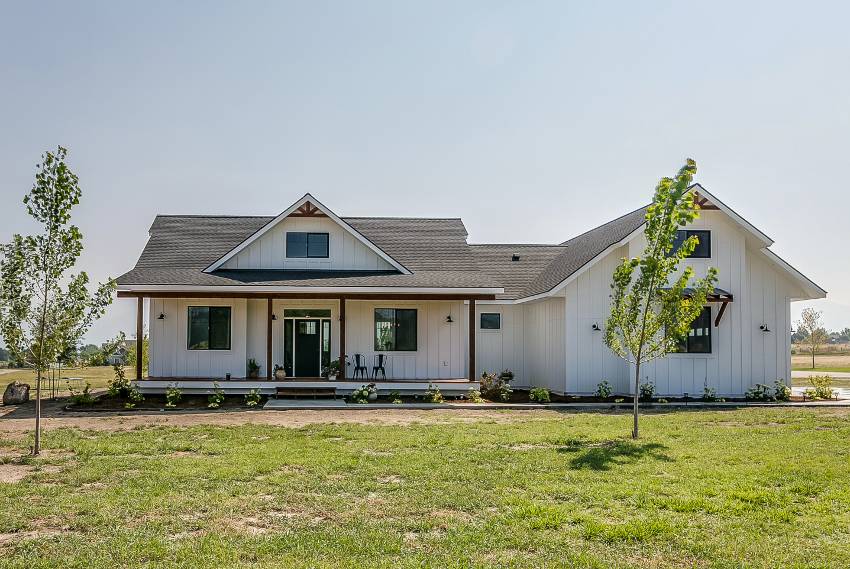 A white ranch home exterior with small trees and a patchy lawn with growing grass on a sunny day 