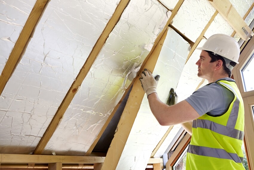 A worker installing rigid insulation boards on roof ceiling