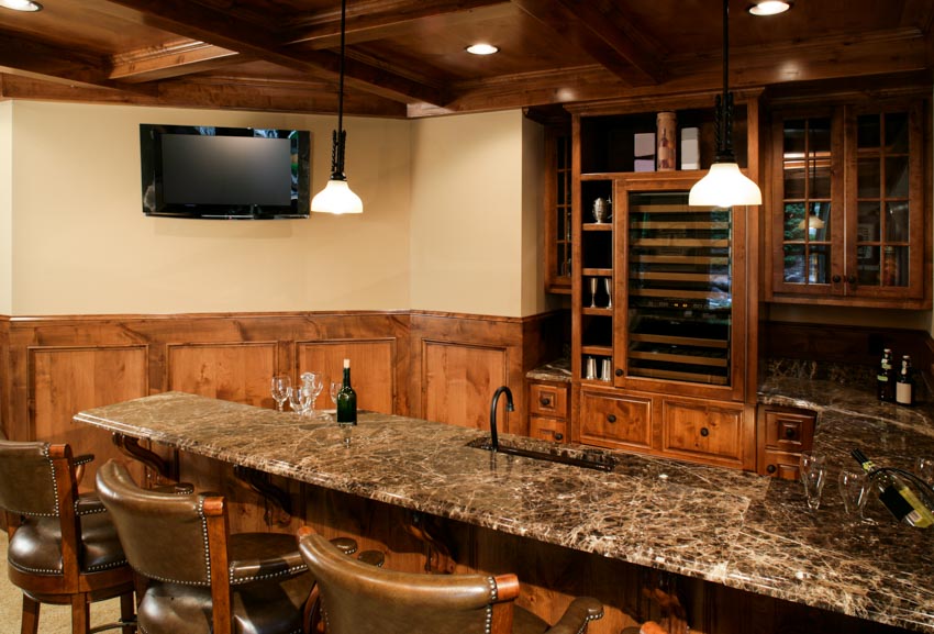 Basement wet bar with granite countertop, solid wood cabinets, hanging lights, wine cooler, and television