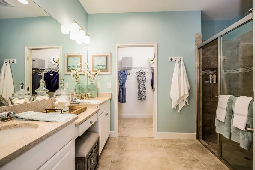 Bathroom with aqua blue walls, countertop, mirror, drawers, glass divider, and shower area