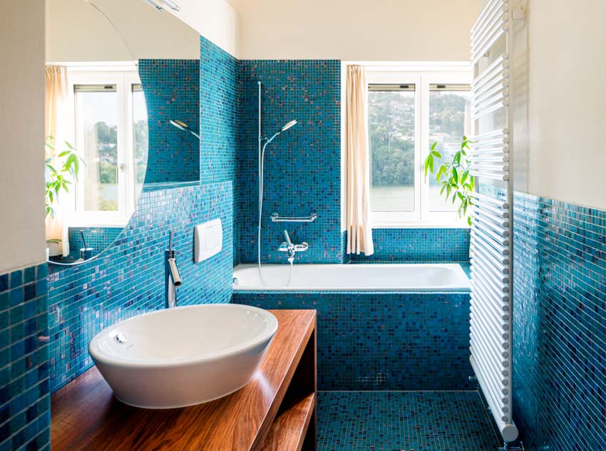 Bathroom with blue glass tile shower, wood vanity, sink, faucet, mirror, and windows