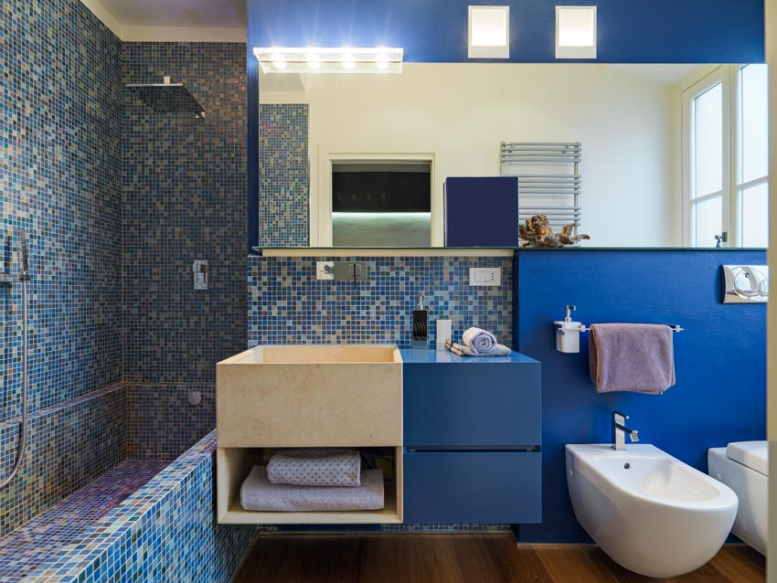 Bathroom with blue tiles, cabinets, mirror and towels